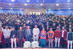 Large group photo in an auditorium with students and faculty standing in rows, front row wearing formal and traditional attire.