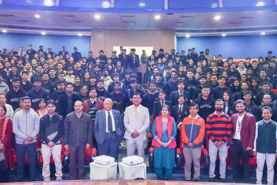 Large group photo in an auditorium with students and faculty standing in rows, front row wearing formal and traditional attire.