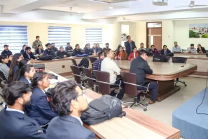 A seminar or lecture in a conference room with students seated around a U-shaped table listening to a speaker at the front.