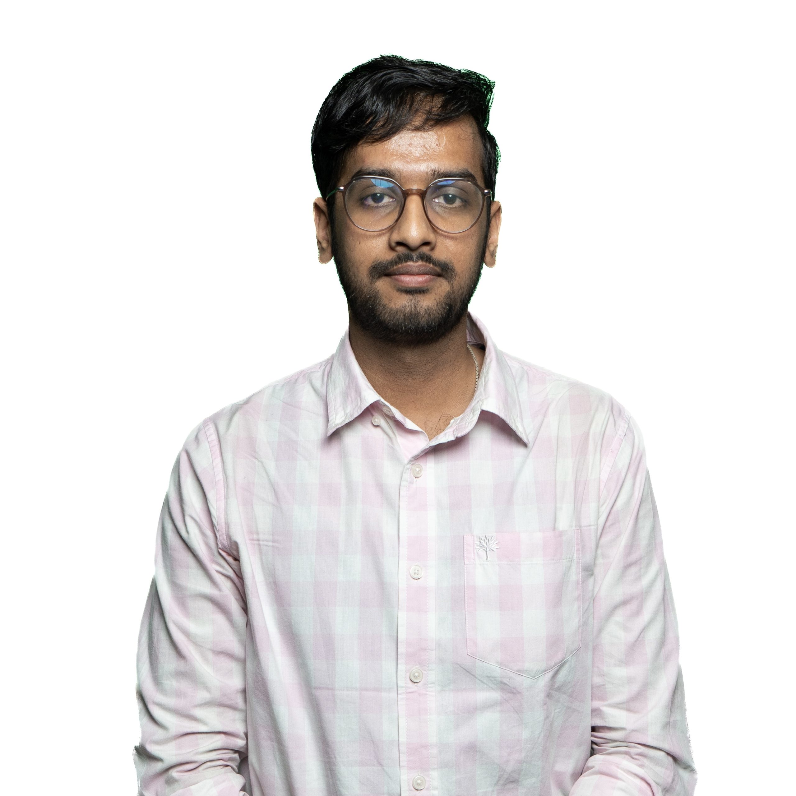 Abhinav_Bahuguna Portrait of a man with dark hair and beard, wearing round glasses and a pale pink plaid shirt against a white background.