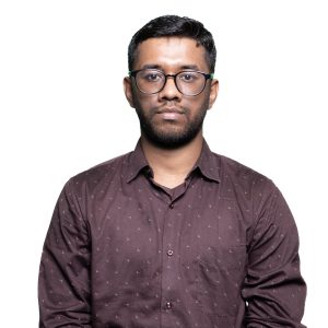 Front-facing man with short dark hair and glasses wearing a maroon patterned shirt against a white background.