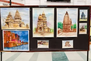 Display board with multiple watercolor paintings of Indian temples pinned outdoors, including tall towered architectures and a riverfront scene.