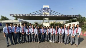Group of students in uniform posing outside NISM entrance, National Institute of Securities Markets building behind them.