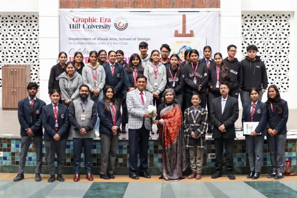 Group of students and staff posing on a stage in front of a Graphic Era Hill University banner; a man presents flowers to a woman in a sari.