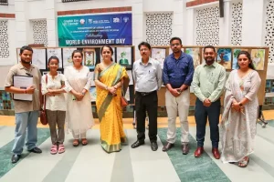 Eight people posing in front of art displays at a World Environment Day event banner above them.