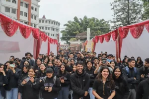Large group of students wearing dark clothing pose for a photo under red festival drapes along white tents outdoors at a campus area.