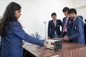 Student in a blue blazer adjusting a power supply on a lab bench while others assemble a circuit at a workspace.