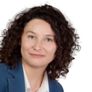 Dr. Ewelina Idziak Professional headshot of a woman with curly brown hair, wearing a blue blazer and white shirt, looking at the camera.