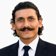 Dr. Raj Kumar Singh Professional headshot of a man with a handlebar mustache in a navy suit and tie, against a white background.