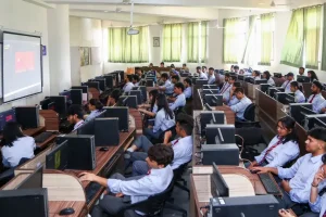 A crowded computer lab with students at rows of desks using desktop PCs at each station in uniform outfits.