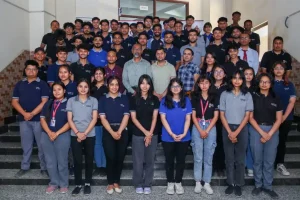 Large group of students or colleagues posing on stairs for a team photo, facing the camera and smiling.
