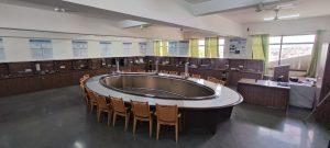 Large circular conference table surrounded by tan chairs in a classroom-style lab, with posters on the walls and a podium by the windows.