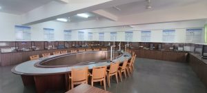 Large conference/training room with a circular central table surrounded by orange chairs, posters on the walls, and built-in cabinets along the back.