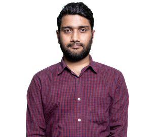 Portrait of a man with dark hair and beard wearing a red plaid shirt against a white background, facing the camera.