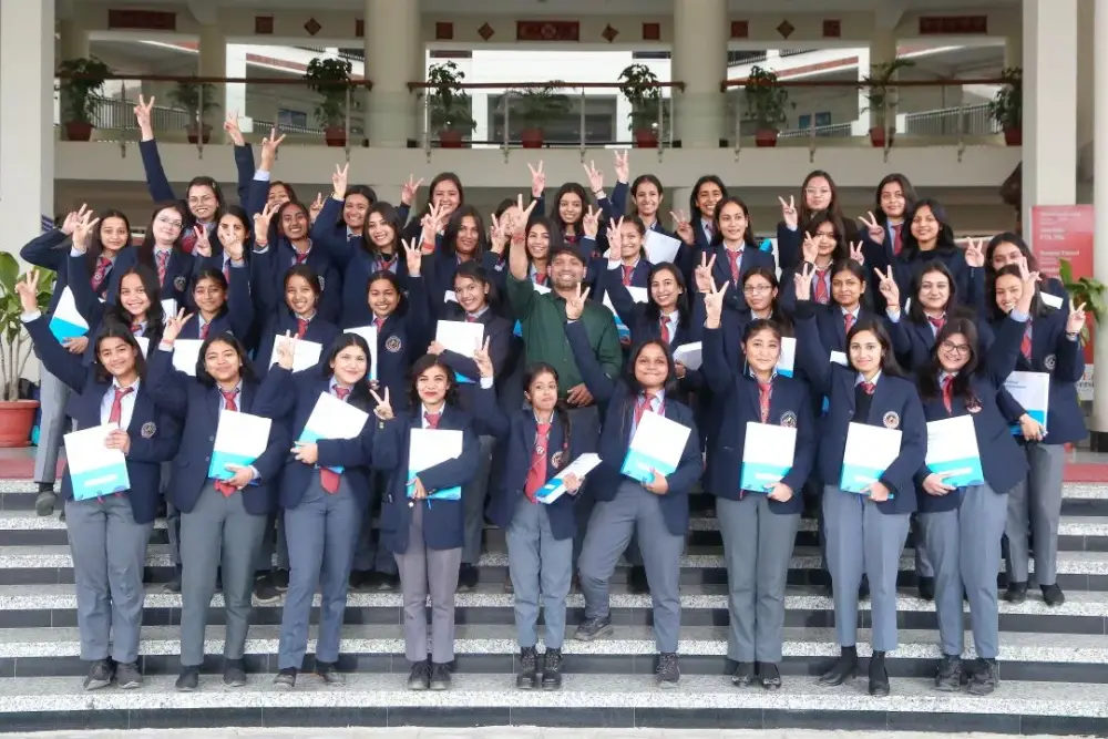 Group of students in navy blazers and red ties pose on stairs, holding blue and white folders.