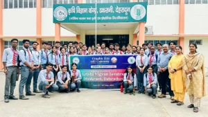 Group of students in gray shirts and red ties pose outside a campus building, holding a banner for a Krishi Vigyan Kendra visit at Graphic Era Hill University, Dehradun.