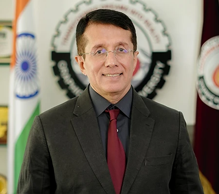 Portrait of a man in a dark suit and red tie, standing in front of a government emblem and flags in the background.