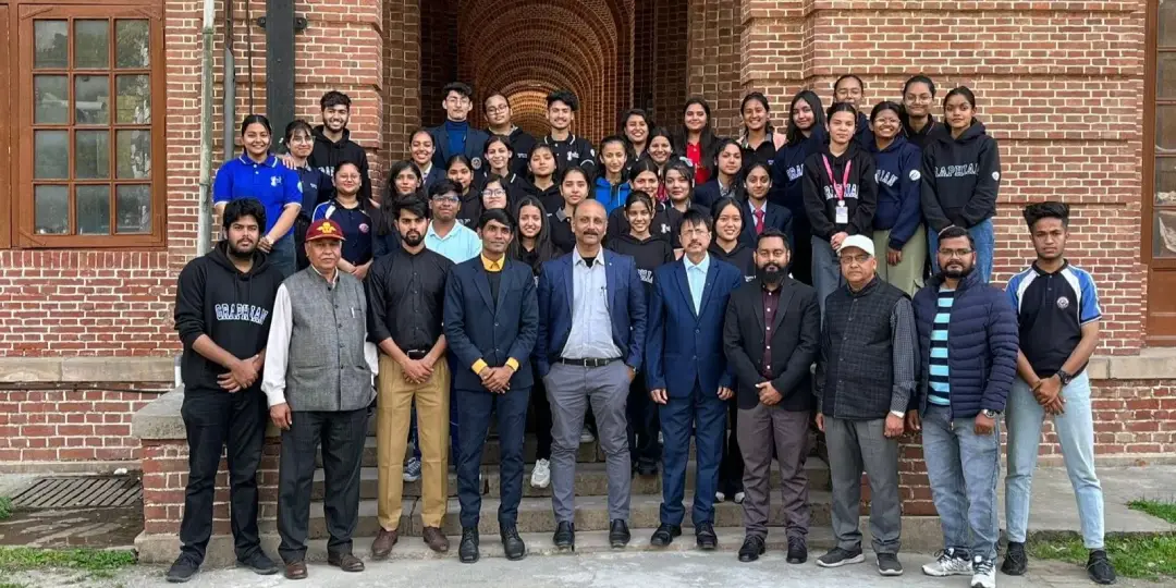 Group of students and instructors posing on steps outside a brick-campus building with arches in the background. - Captures a large, diverse group for a class or program photo.