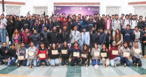 Large group of students posing with certificates and trophies during an award ceremony in a hall, banner visible in the background.