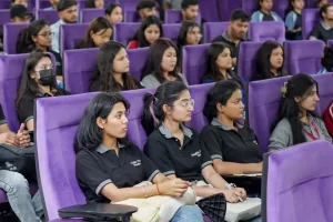 Group of students sitting in purple theater-style seats, attentively listening in a lecture hall.