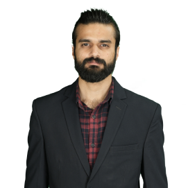 Man with dark hair and beard wearing a black blazer over a red plaid shirt, looking at the camera.