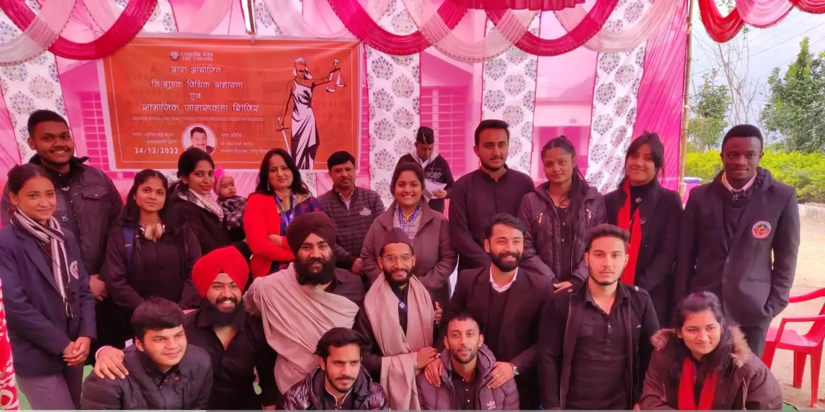 Group of men and women posing for a photo at a community event under a pink tent, with a banner in the background.