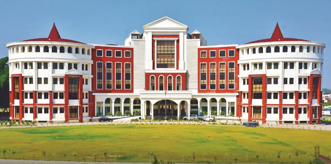 Front view of a large red-and-white university building with rounded towers, central entrance, and a green lawn.