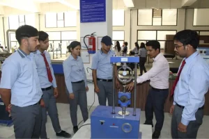 Group of students in uniform watching a blue material testing machine during a lab demonstration in a workshop area.