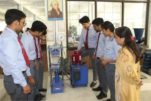 Group of students in uniform observe a blue and red laboratory testing machine during a demonstration inside a workshop.