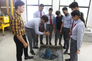 Group of students in school uniforms watch as a classmate operates a tool into a blue specimen in a lab tray.
