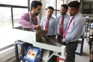 Four male students in shirts and red ties watch a man operate a metalworking machine in a bright lab.