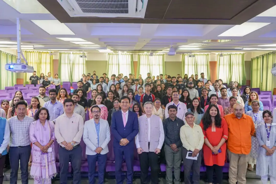 Large diverse group posing for a group photo in an auditorium with purple seats and green curtains (front row in business attire).