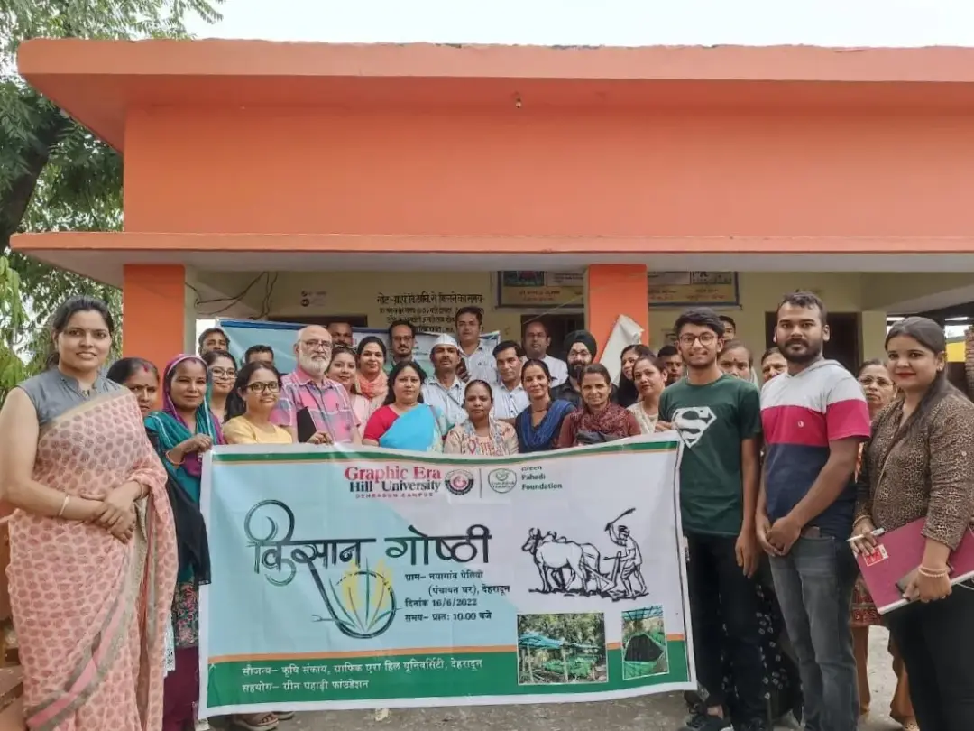 Group of men and women posing outdoors with a large banner for a community event at Graphic Era Hill University.