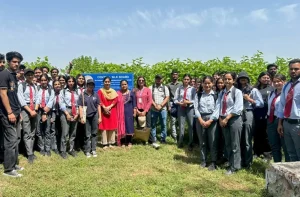 Group of students in uniforms and a few adults posing outdoors beside a blue signboard on a sunny day since field trip